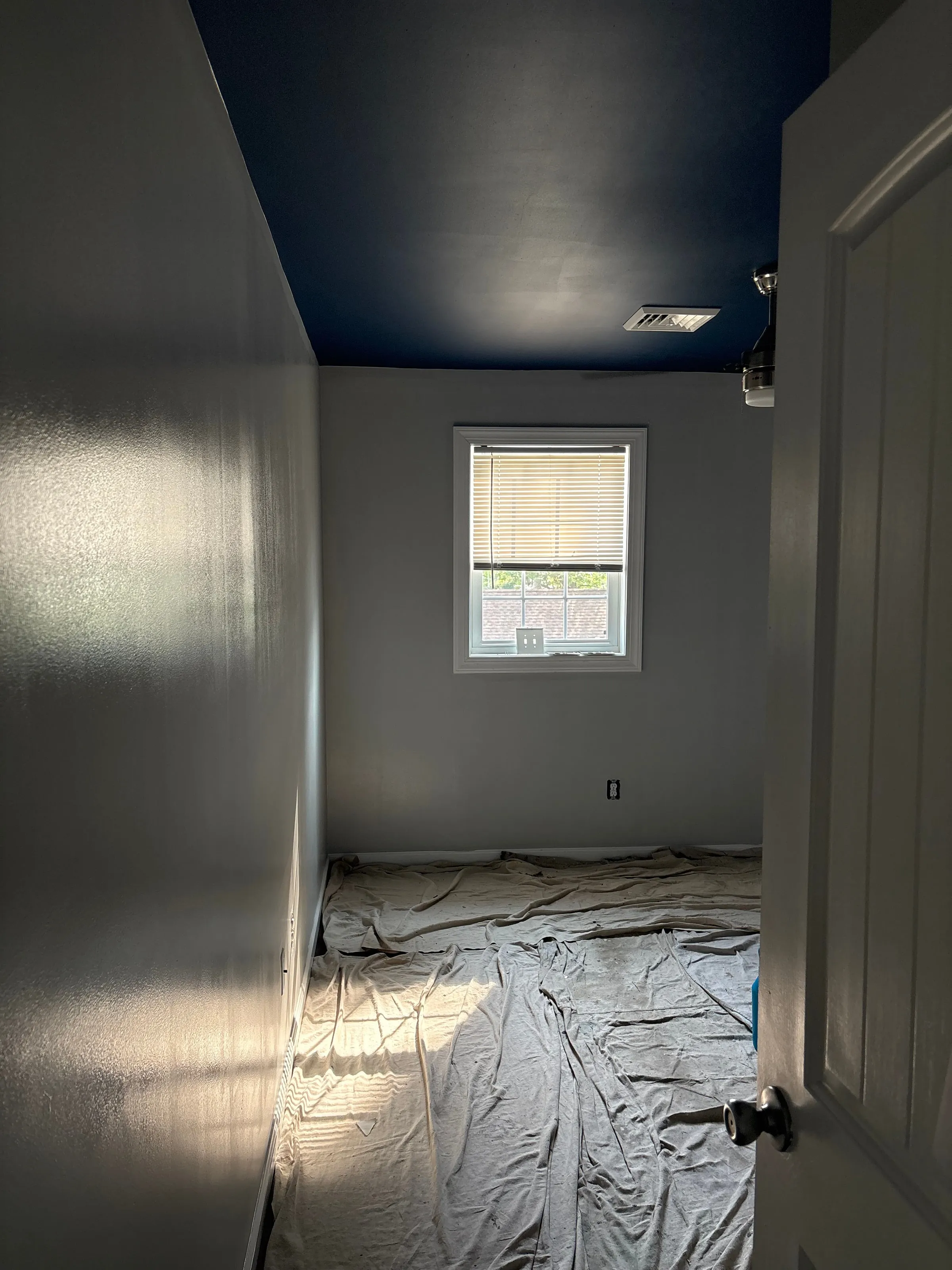 Room with a deep navy painted ceiling and drop cloths covering the floor