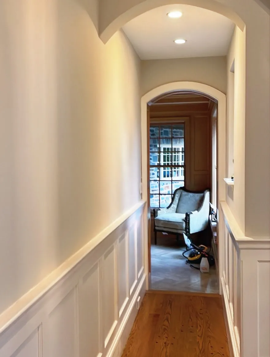 Hallway with painted wainscoting leading to an arched doorway